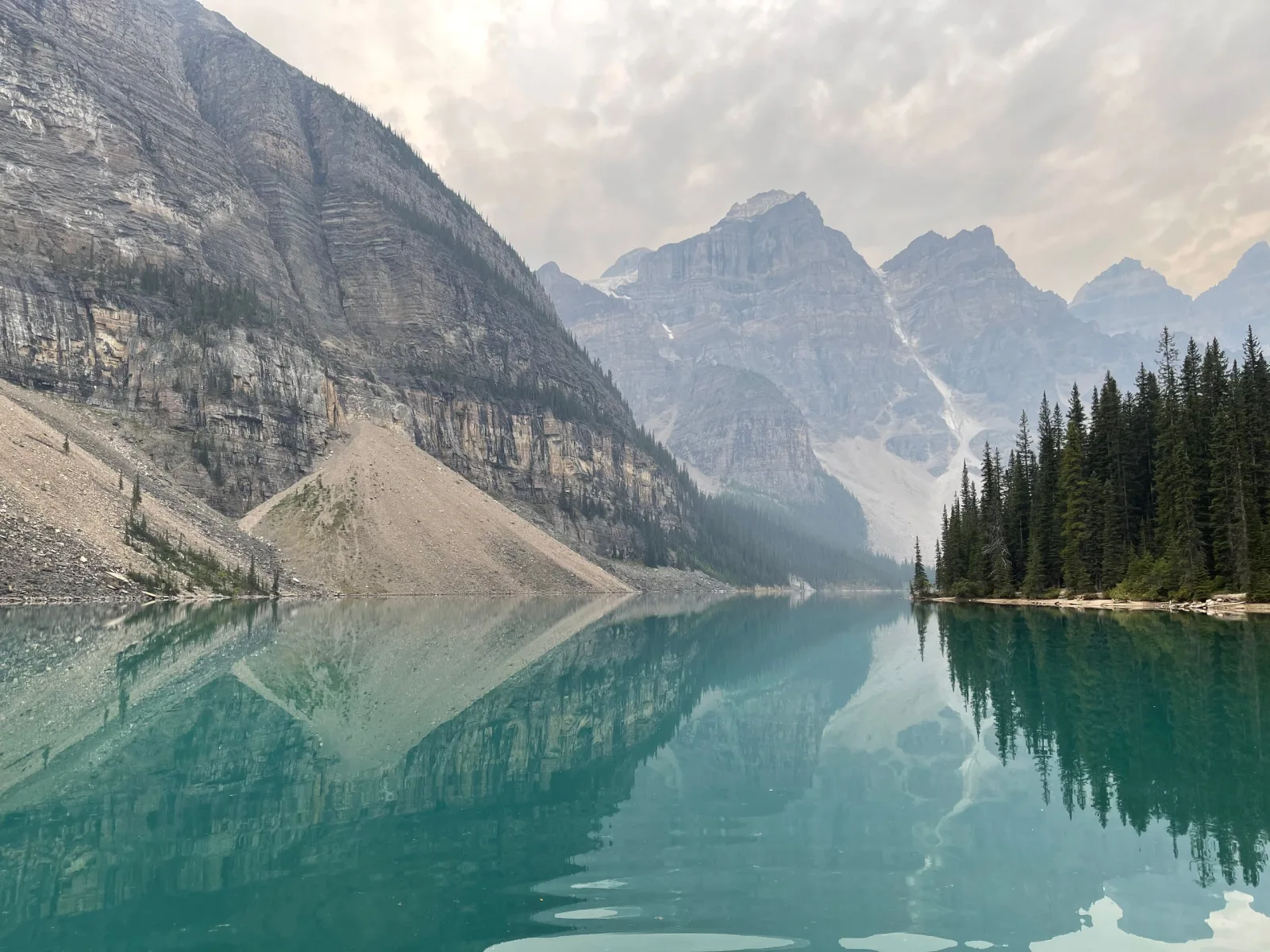 Turquoise lake reflecting steep mountains and evergreen trees in Alberta.