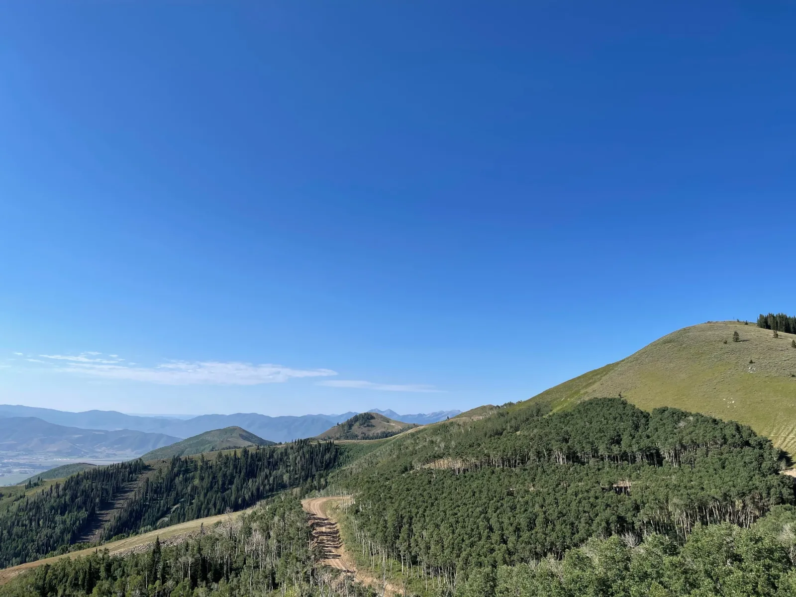 A trail following a green Utah ridgeline above distant mountain valleys.