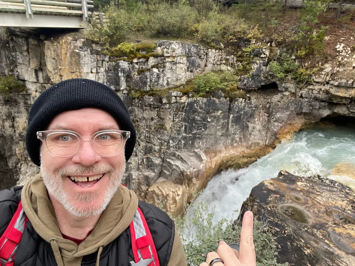 David smiling beside a waterfall flowing through a rocky gorge in British Columbia.